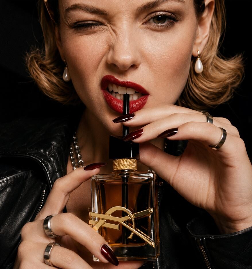 She bites the perfume bottle with a wink